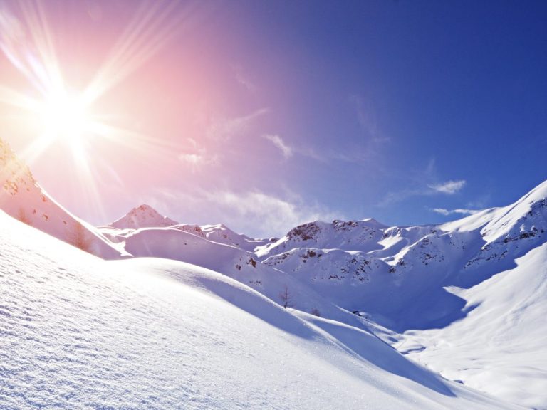 Helle Sonneneinstrahlung auf schneebedeckten Bergen unter klarem Himmel.