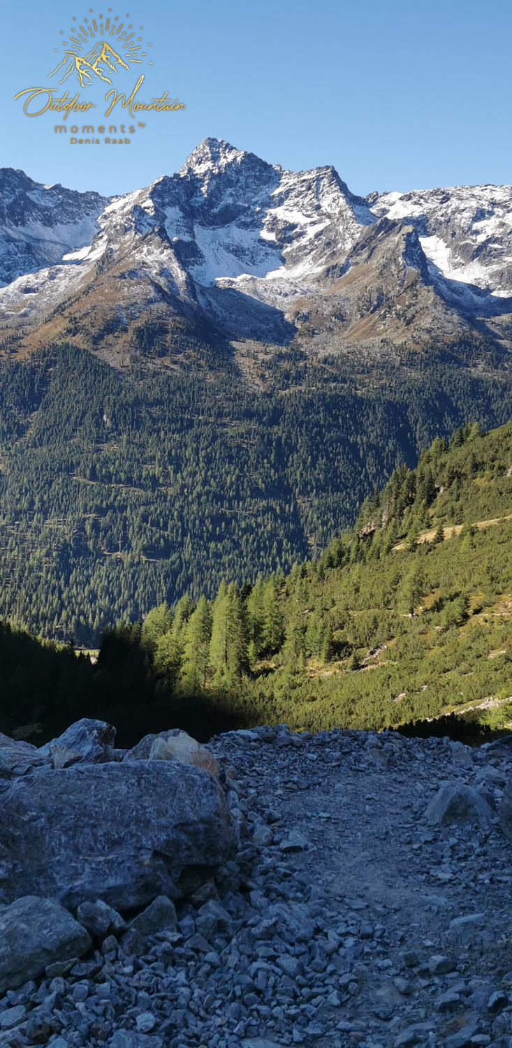 Berglandschaft mit schneebedeckten Gipfeln und grünen Hügeln im Vordergrund.